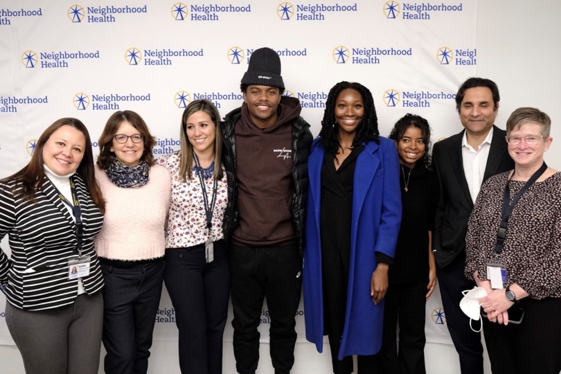 A diverse group of people standing in front of a Neighborhood Health Sign