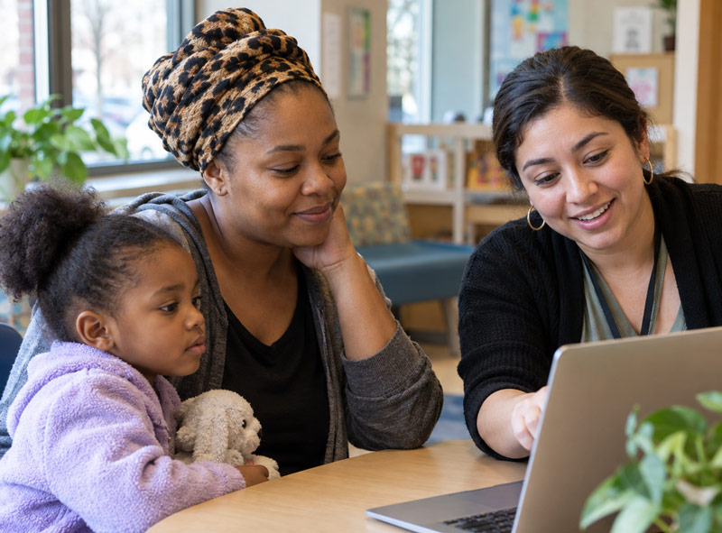 Mom and daughter looking at a laptop with lady helping