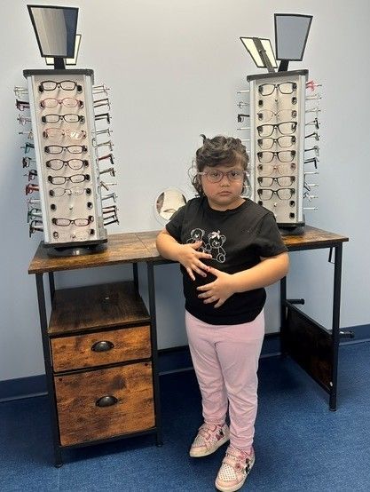 Young patient wearing new glasses next to eyeglass frame displays at Arlington Pediatric Center